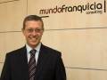 Hombre sonriente en traje de negocios frente a un fondo con el logotipo de 'mundoFranquicia consulting'.