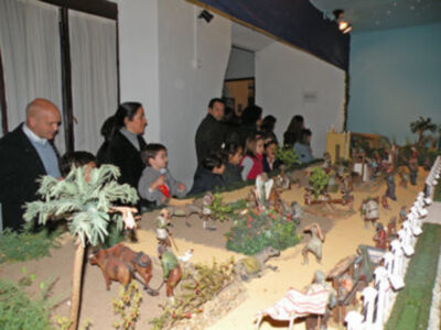 Una escena en miniatura de una aldea medieval con figuras humanas y animales en un entorno verde y arena.