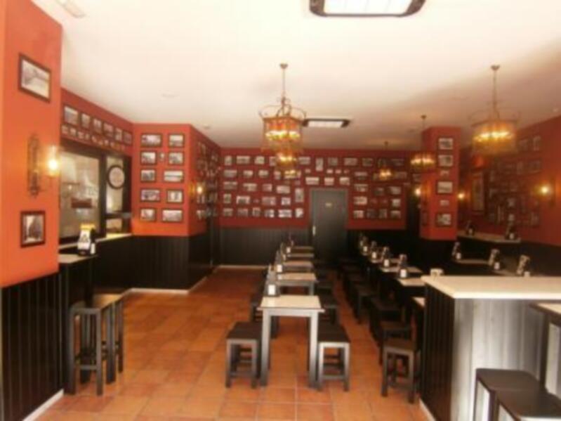 Interior of a cozy restaurant with red walls, black paneling, and framed photos, featuring tables and bar seating.