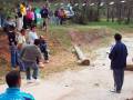 Un grupo de personas participando en un juego de pelota con una canasta. La escena está rodeada por árboles y un camino de tierra.