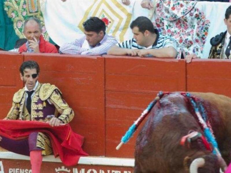 Un torero en traje tradicional sostiene una capa roja mientras un toro se prepara para la matanza en una plaza de toros.
