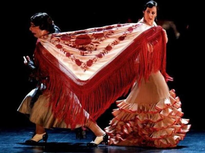 Damas en trajes tradicionales de flamenco bailando sobre un escenario.