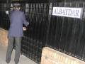 Un hombre en traje aprieta la puerta de un edificio con el nombre 'ALBAYDAR' en una placa azul.