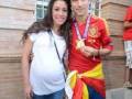 Una mujer embarazada posa junto a un hombre vestido con una camiseta de fútbol española, sosteniendo una bandera nacional.