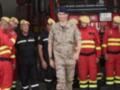 Un grupo de bomberos en uniforme rojo y amarillo, junto a un oficial militar en camuflaje.