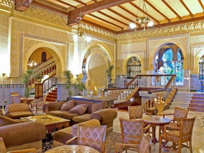 Sala de estar con sofás, mesas y sillas. Decoración árabe con detalles dorados en el techo.