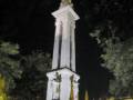 Monumento histórico iluminado en la noche, con detalles dorados y árboles alrededor.