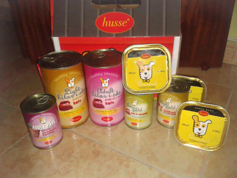 Pack de alimentos para perros Husse, incluyendo latas y envases de pate, con etiquetas de salud y estilo de vida saludable.