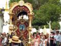 Una procesión religiosa en un ambiente festivo, con una carroza ornada y una multitud vestida de colores.