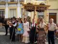Una familia vestida con trajes tradicionales posa frente a una carroza de fiesta, rodeada por flores y decoraciones festivas.