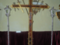 Cruz procesional con instrumentos de trabajo y estandartes en un entorno religioso.