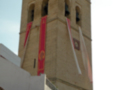 Torre con banderas rojas y blancas, edificio blanco a la izquierda.