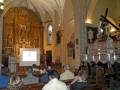 Interior de una iglesia con un altar grande y vitrales. Una persona está presentando en un proyector en el centro de la imagen. La arquitectura es típica con columnas y bóvedas altas.