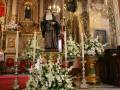 Interior de una iglesia con un altar adornado con flores blancas, velas y estatuas religiosas.