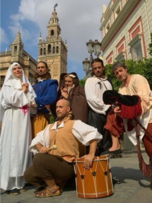 Grupo de personas vestidas con trajes medievales posando frente a la Giralda en Sevilla.