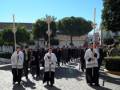 Una procesión religiosa con personas vestidas de blanco y negro, sosteniendo cruces y caminando en una calle pavimentada.