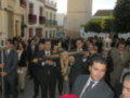 Una procesión religiosa en un entorno histórico, con personas vestidas formalmente y portando cruces. En el fondo, se observa una torre de la iglesia de San Miguel Arcángel.