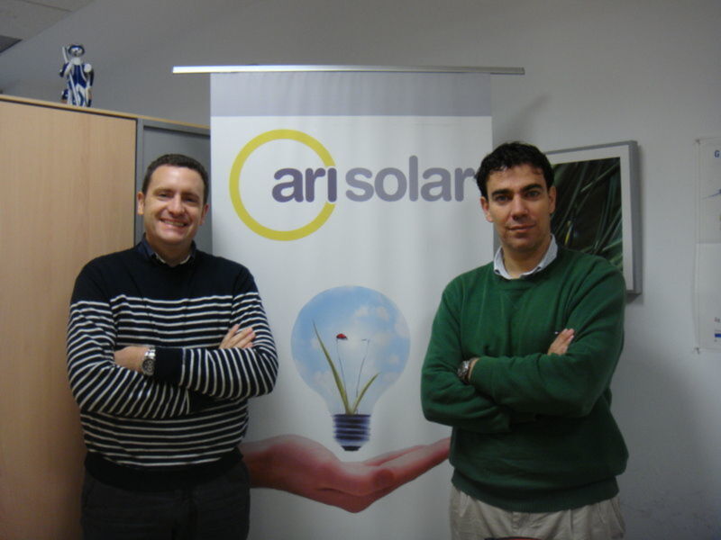 Dos hombres sonrientes en frente de un banner con el logo de Arisolar.