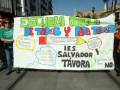 Un grupo de personas sostiene un cartel gigante que afirma "Escuela pública de todos y para todos". El cartel menciona la I.E.S. Salvador Tavora y promueve el derecho a la educación pública, destacando que "hacemos política del aprendizaje de las almas". También se menciona la importancia de "recursos educativos, programas y prácticas" para mejorar la educación.