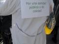 Person wearing a white coat with a sign that reads 'Por una sanidad pública y de calidad' on the back.