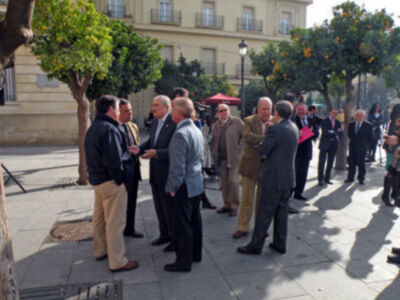 Gente conversando en la calle, árboles y edificio al fondo.