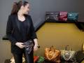 Una mujer en un traje negro está seleccionando una bolsa de mano entre varias opciones dispuestas sobre un mostrador.