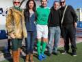 Una familia feliz posando para una foto en un campo de fútbol. La madre y la hija están vestidas con ropa casual, mientras que el padre y el hijo están en ropa deportiva con una camiseta verde y pantalones cortos blancos.