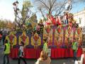 Desfile de carros alegóricos durante un festival de carnaval en una plaza decorada con árboles y edificios históricos.