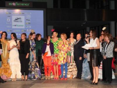 Una escena en un desfile de moda flamenca con modelos vestidos en trajes tradicionales y una pantalla de fondo.