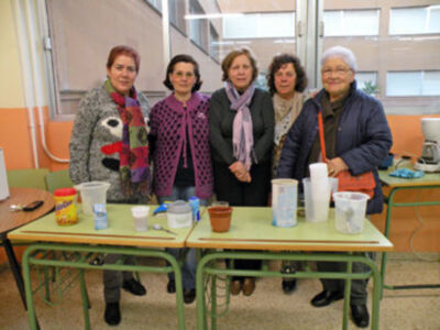 Las personas están en una escuela o centro educativo, posiblemente durante un evento escolar. La mesa tiene varios recipientes de alimentos y bebidas, indicando una actividad comunitaria o alimentación. Las personas parecen estar en un ambiente educativo, posiblemente una escuela o centro de enseñanza.