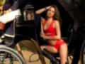 Una mujer vestida con un bikini rojo y medias negras se sienta en el asiento trasero de una carruaje. Detrás de ella, un hombre con sombrero y traje se sienta en el asiento delantero. La escena está ambientada al aire libre, con un fondo de edificios antiguos.