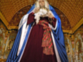 Estatua de una figura histórica vestida con un manto rojo y azul, posiblemente de una persona importante o religiosa. La imagen se encuentra en un entorno arquitectónico con detalles dorados y una bóveda de madera.