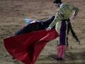 Un torero en traje de luces y capa roja se prepara para enfrentarse al toro en un ruedo de arena.