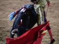 Un torero lidiando un toro en una corrida de toros, con el capote rojo en movimiento.