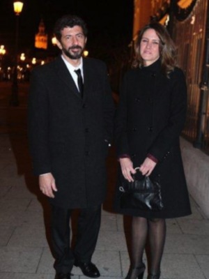Dos personas vestidas con abrigos oscuros caminan por una calle iluminada de noche, posiblemente en un evento formal.