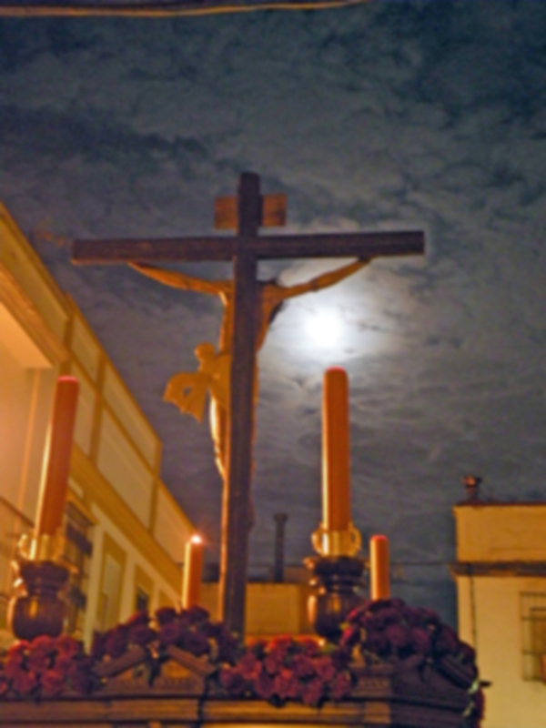 Crucifijo de madera en un entorno nocturno con una luna llena en el cielo.