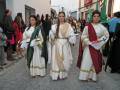 Procesión con vestimentas tradicionales en una calle de pueblo, con participantes en trajes históricos.