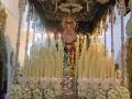 Una imagen de una Virgen en un altar ricamente decorado con velas y flores blancas, iluminada por luces doradas.