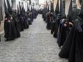 Una procesión religiosa en una calle adoquinada, con participantes vestidos de negro y portando capas largas.