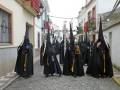 Cofrades en trajes tradicionales marchando por una calle adoquinada.