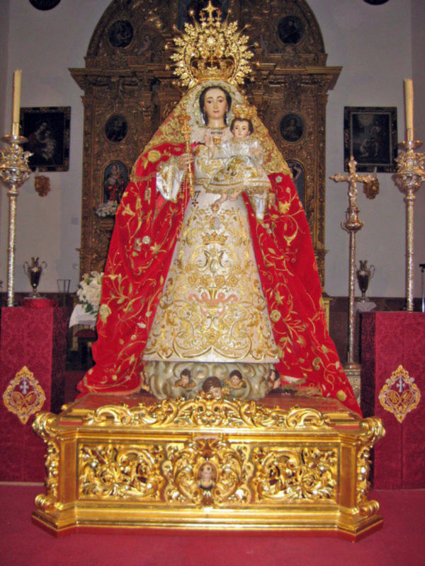 Imagen de la Virgen María en un altar dorado, rodeada por candelabros y cuadros.