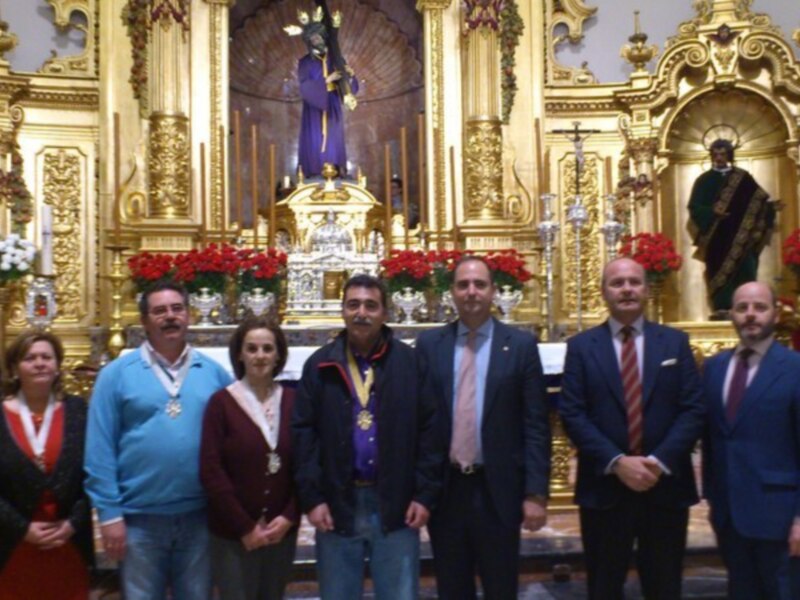 En una iglesia llena de dorado y luces, un grupo de personas posa frente a un altar con una imagen central. La decoración dorada y las flores rojas en el fondo crean un ambiente festivo.