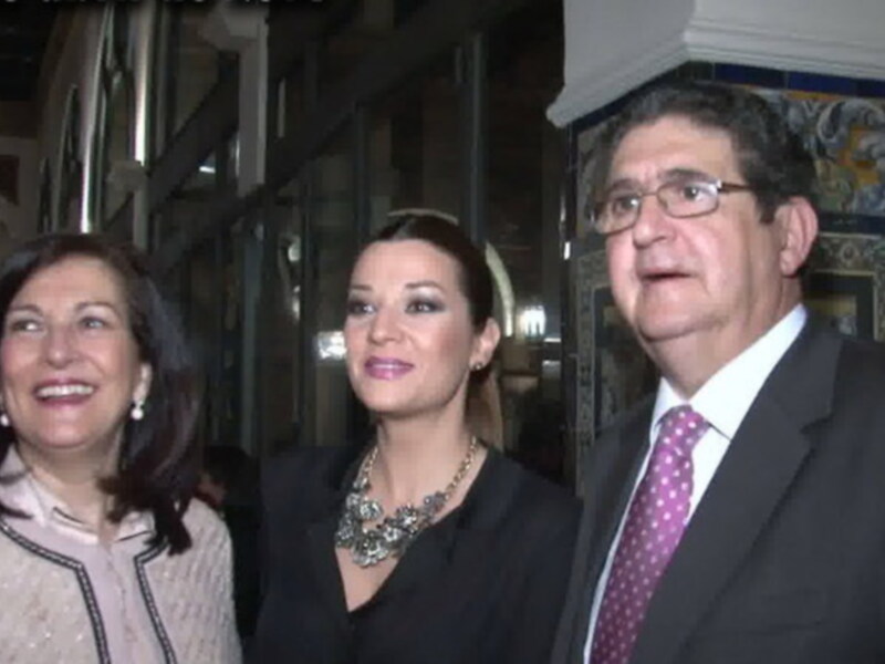 Tres personas posando en una calle iluminada por faroles, con un edificio de estilo clásico en el fondo.