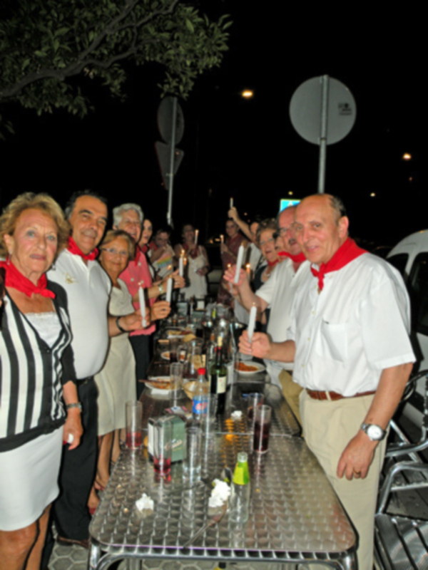 Celebración nocturna al aire libre con personas en trajes formales, posando junto a una mesa con velas y bebidas.
