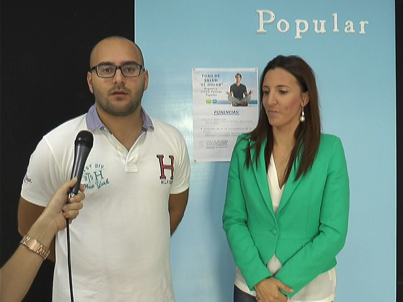 Dos personas, una con un polo blanco y la otra con una chaqueta verde, frente a un fondo azul con un cartel informativo. La imagen parece ser de una presentación o conferencia, posiblemente relacionada con el sector financiero.