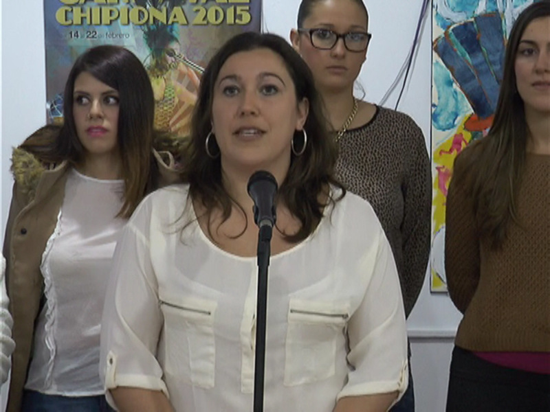 Las tres mujeres están en una conferencia o presentación, con una de ellas hablando al micrófono. La imagen muestra detalles como sus vestimentas y el fondo con carteles informativos.
