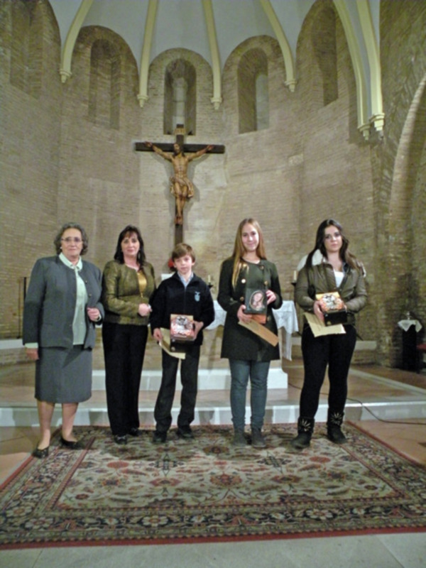 Una imagen de cinco personas posando frente a un crucifijo en una iglesia con arcos y columnas blancas. La escena está iluminada por la luz natural de la ventana.