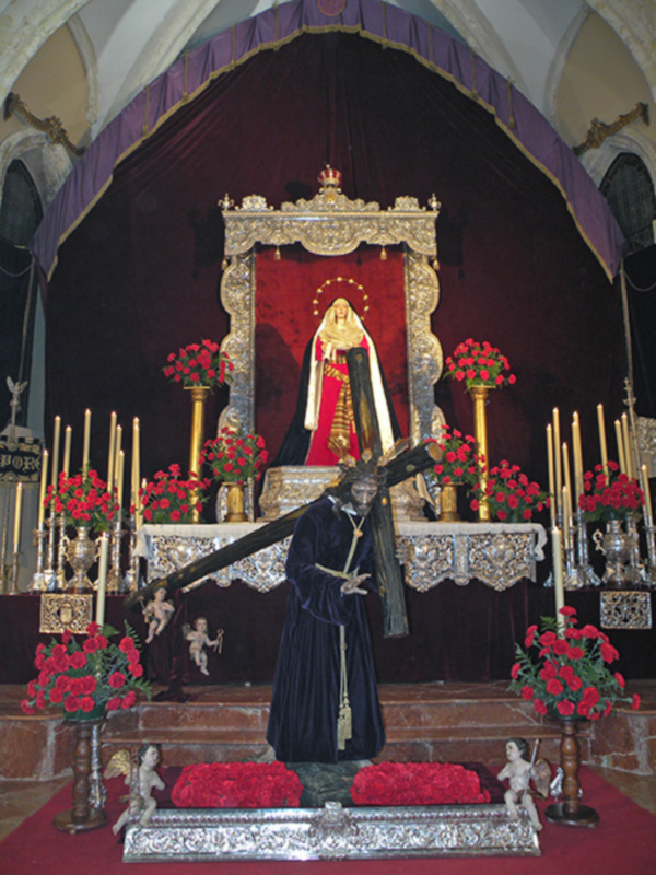 Interior de una iglesia con un altar central, estatuas religiosas y flores rojas.