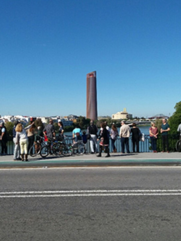 Grupo de personas disfrutando de una vista panorámica junto al río Guadalquivir en Sevilla, con la Torre Sevilla al fondo bajo un cielo azul claro.