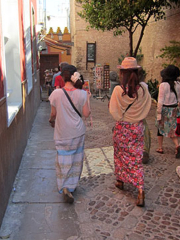 Un grupo de personas camina por una calle adoquinada en un entorno urbano con edificios de fachadas coloridas y árboles.